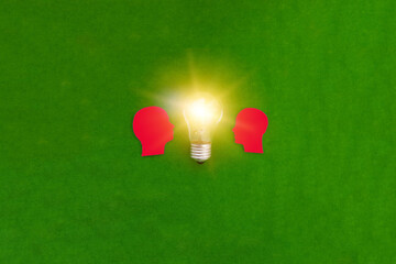 Two silhouettes of a red man's head look at an electric light bulb on a green background. The concept of joint ideas.