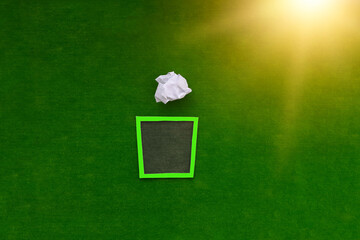 A crumpled sheet of white paper falls into the trash can on a green background. The concept of removing excess, recycling.