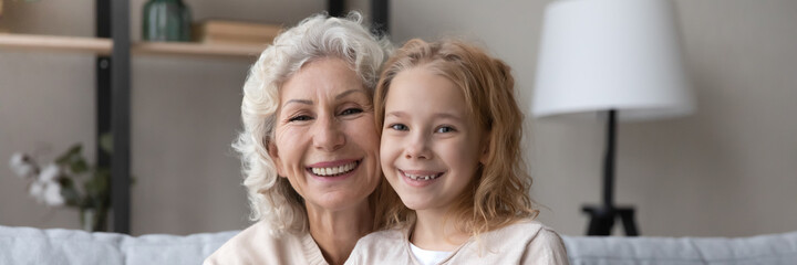 Horizontal banner photo head shot close up view bonding hoary older senior woman posing with joyful adorable kid girl, enjoying tender carefree moment at home, loving family relations concept.