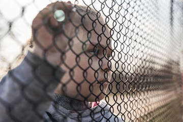 Little girl with a sad look behind a metal fence, social problems, raising children in orphanages