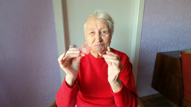 Dental concept. Elderly female 90 years old inserts denture. Senior woman gray hair using dental prosthesis on gray background. Old patient fitted artificial jaw in studio. Flexible nylon denture