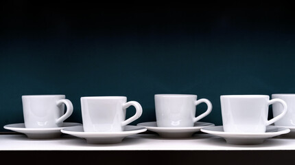 White coffee cups with saucers on a dark green background.
