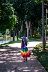 A little girl in a rainbow dress fun runs on the concrete path in the park.