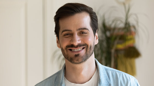 Head shot of millennial generation attractive guy in casual wear standing indoor pose on camera. Confident handsome businessman, successful happy young bearded 35s male portrait with wide toothy smile