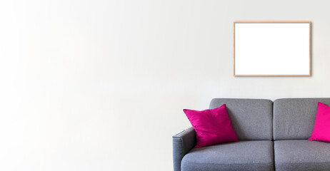 Empty wooden picture frame on a white wall above a sofa. Horizontal banner