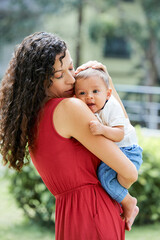 Young woman with long curly hair holding her little son and stroking his head softly