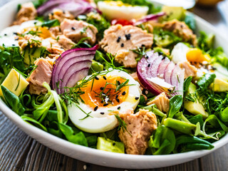 Tuna salad - tuna, avocado, hard boiled eggs, cherry tomatoes, lettuce and onion on wooden table

