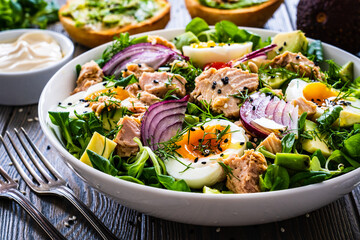 Tuna salad - tuna, avocado, hard boiled eggs, cherry tomatoes, lettuce and onion on wooden table
