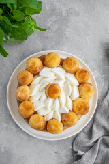 Saint Honore cake with profitrols, caramel, custard and whipped cream on a white plate on a gray concrete background. Traditional French dessert. Copy space.