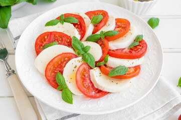 Classic caprese salad with mozzarella cheese, tomatoes and basil on a white plate on a wooden background. Top view, copy space.