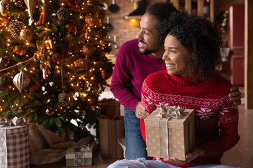 Fototapeta na wymiar Smiling African American couple celebrate Christmas at home look in distance dream of happy future together. Smiling biracial man and woman enjoy New Year winter holidays make wish visualize.