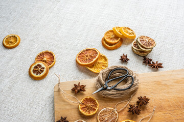 Weihnachtsschmuck getrocknete Orangenscheiben und Anis, Flatlay mit Schere Bindfaden und Holzablett