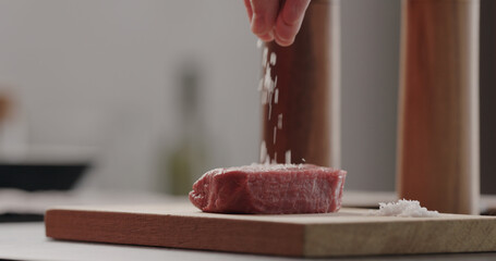 salting beef steak on wood board with sea salt flakes