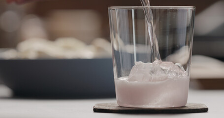pour rose water over big ice rock into tumbler glass