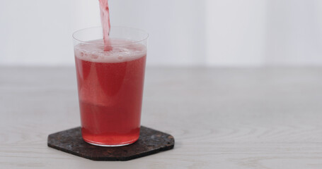 pour berry water over big ice rock into tumbler glass