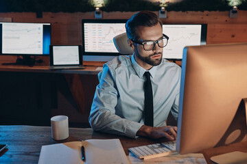 Concentrated young man working on computer while staying late in the office