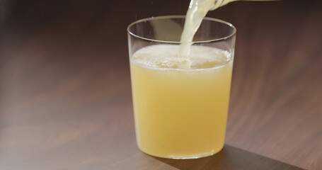pour orange juice from glass bottle into tumbler glass on walnut table