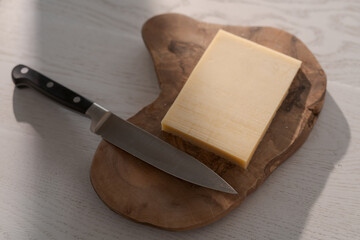Small block of aged cheese on wood board with knife