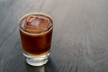 Espresso tonic with clear ice cube in tumbler glass on oak wood table with copy space
