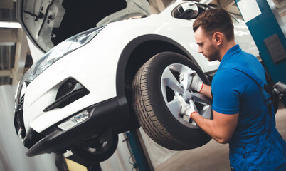 Handsome professional car mechanic changes a wheel on a car or carries out a tire change at a...