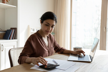 Household budget. Young indian female sit at table calculate utility payments before make money...