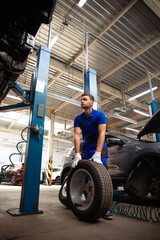 Handsome professional car mechanic changes a wheel on a car or carries out a tire change at a specialized auto repair center