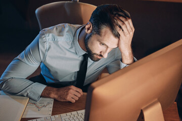Top view of frustrated young man holding head in hand while staying late in the office
