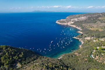 View from above, stunning aerial view of a bay with boats and luxury yachts sailing on a turquoise, clear water surrounded by cliffs. Porto Santo Stefano, Monte Argentario, Italy.
