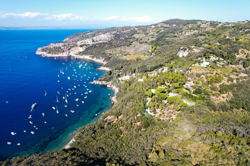 Fototapeta premium View from above, stunning aerial view of a bay with boats and luxury yachts sailing on a turquoise, clear water surrounded by cliffs. Porto Santo Stefano, Monte Argentario, Italy.