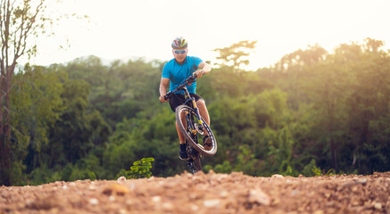 Fototapeta na wymiar Mountain bikes cyclist cycling, Asian man athlete riding biking jumping on rocky terrain trail, extreme sport wear gear uniform helmet, exciting freedom outdoor sunset nature healthy active lifestyle