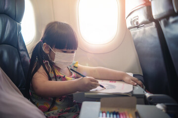 Obraz premium Adorable Asian young girl traveling commuting on plane transportation wearing surgical facemask protection from COVID-19 coronavirus, commercial airline services, happy joyful in evening sunset.