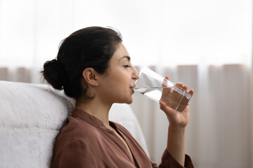 Drinking water. Side view young indian woman enjoy pure fresh cool mineral water at morning. Profile shot of thirsty millennial mixed race lady hold glass swallow crystal still aqua with closed eyes - Powered by Adobe
