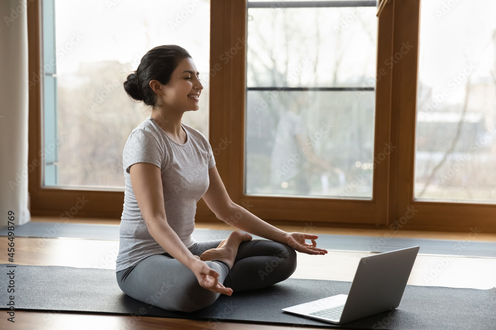 Wall mural yoga online. happy young indian female yogi do exercises before laptop screen at home or in gymnasti