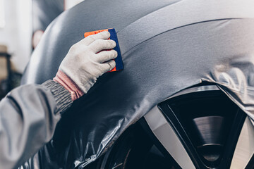 Car wrapping specialist putting vinyl foil or film on car. Selective focus. .