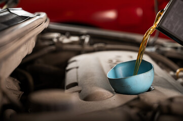 Auto mechanic pours oil into a car engine.