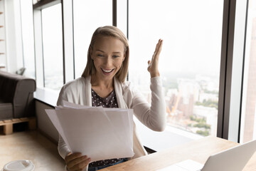 Overjoyed millennial Caucasian female employee read good promotion news in paper letter or correspondence. Smiling young woman triumph feel euphoric with message in paper document.