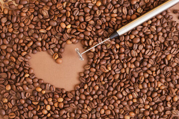 heart made of coffee beans and metal handheld milk steamer on brown background. Handheld frother or...