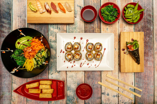 Top view image of sushi and asian food. Salmon poke bowl with wakame salad, edamame in pods, uramaki shrimp roll in tempura with nori seaweed. Smoked eel, shrimp and avocado nigiri