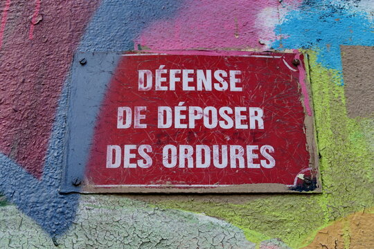 D&eacute;fense de d&eacute;poser des ordures. Panneau lettrage blanc sur fond rouge pos&eacute; sur une fa&ccedil;ade avec graffitis..
