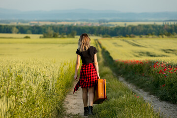Young girl with suitcase walking down the road on countryside