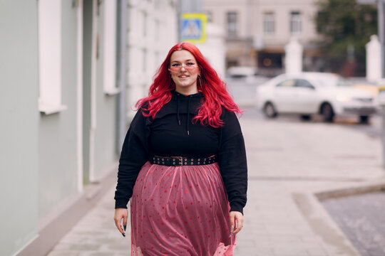 European plus size woman. Young red pink haired body positive girl walk at city street outdoors