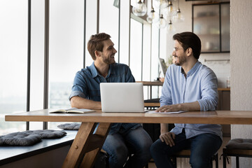 Overjoyed millennial Caucasian male employees have fun laugh working together on computer in...