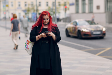 Fototapeta premium European plus size woman walking outdoor street city with mobile cellular phone. Young red pink haired body positive girl using cellphone smartphone
