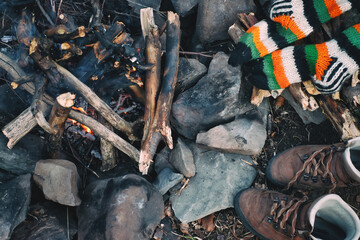 Knitted socks and hiking boots drying near a campfire