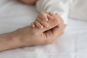 New mom holding little hand of sleeping newborn baby. Mother comforting infant resting in bed, touching arm of little son or daughter with love, care, tenderness. Bonding, childbirth concept. Close up