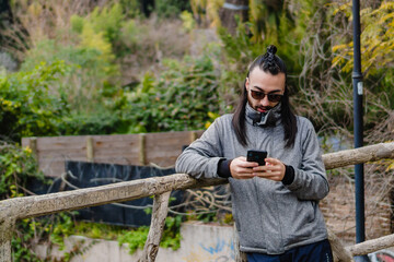 young hispanic latino man chatting on his smart phone in an open-air park, sports clothing