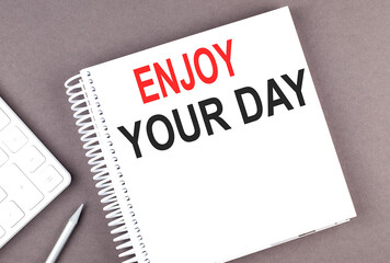 ENJOY YOUR DAY text on the notebook with calculator and pen
