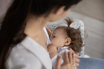 New mother breastfeeding adorable child, sitting, holding baby in arms. Young mom feeding cute...