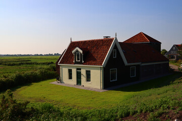 Fototapeta na wymiar Dutch country house in a field, white walls, red tiled roof, green grass. Big house close up photo. Countryside landscape of the Netherlands. 