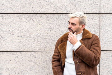 thoughtful man with hand to chin, standing on the background of a wall, looking up for an idea,...
